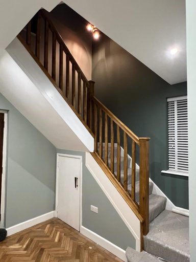 Stairs with wooden railing and a green wall, featuring carpeted steps and a small door below.