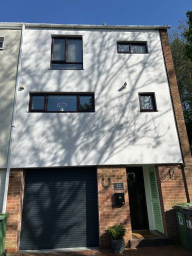 Modern three-storey house with a garage, surrounded by trees casting shadows.